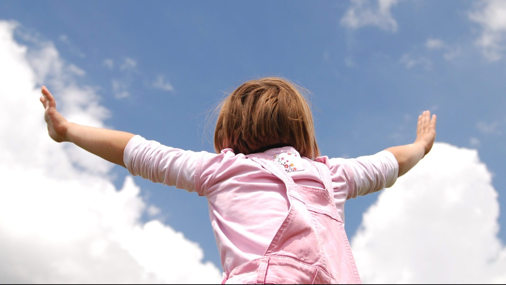 Blog BusinessKids, niña con los brazos abiertos, con el cielo azul de fondo.